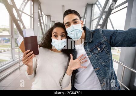 La pandémie se déplace. Un couple arabe excité en masques médicaux prenant Selfie à l'aéroport Banque D'Images