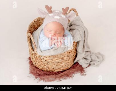 Portrait d'un nouveau-né bébé garçon portant un chapeau tricoté avec des cornes de cerf dormant sur son ventre dans le panier et tenant les petites mains sous ses joues. adorable inf Banque D'Images