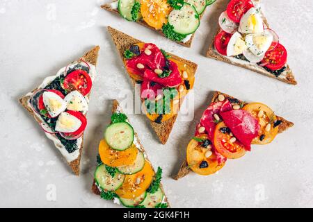 Toasts de grains entiers frais avec des ingrédients sains - prosciutto, tomates, oeufs, et légumes. Sandwich à la bruschetta italienne, légumes verts et graines sur le dessus Banque D'Images