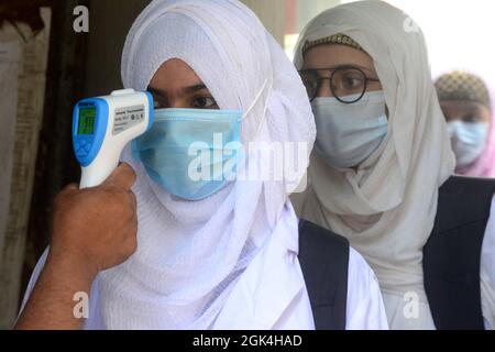 Un fonctionnaire vérifie la température corporelle d'un étudiant à son arrivée à l'école et au collège des filles du gouvernement d'Azimpur à Dhaka, au Bangladesh, le sept Banque D'Images