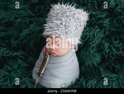 Nouveau-né dans un chapeau ethnique dormant avec un poignard sur fond vert Banque D'Images