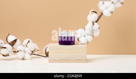 produits cosmétiques dans un pot en verre violet avec un support de couvercle gris sur un podium en bois fait de cubes. Vierge pour les produits de marque, hydratant sur le dos beige Banque D'Images