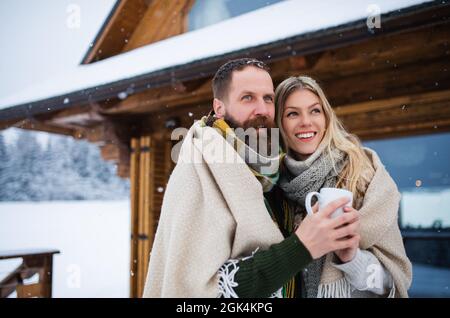 Portrait d'un heureux couple d'âge mûr amoureux appréciant des vacances dans la cabane de montagne, debout à l'extérieur. Banque D'Images