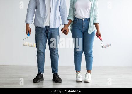 Rénovation, décoration et peinture. Couple afro-américain avec des rouleaux de peinture posant dans leur nouvel appartement, récolte Banque D'Images