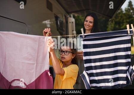 Mère avec fille pendant des vêtements en voiture à l'extérieur en camping, caravane vacances en famille. Banque D'Images