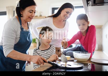 Petites filles heureuses avec la mère et la grand-mère faire des crêpes à l'intérieur à la maison, la cuisine. Banque D'Images