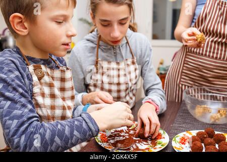 Bonbons de cuisine familiale dans la cuisine maison. Garçon et fille avec leur mère font des bonbons sains avec des fruits et du cacao. Banque D'Images