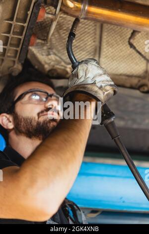 Gros plan d'un jeune homme, mécanicien automobile masculin dans des salopettes faisant le service de voiture à la gare, garage, intérieur. Concept du travail, de la profession, des affaires Banque D'Images