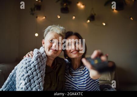 Portrait d'une mère âgée heureuse avec une fille adulte à l'intérieur à la maison, regardant la télévision. Banque D'Images