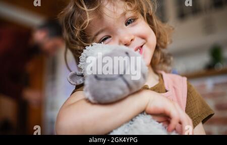 Portrait d'une petite fille mignonne tenant le jouet à l'intérieur à la maison, regardant l'appareil photo. Banque D'Images