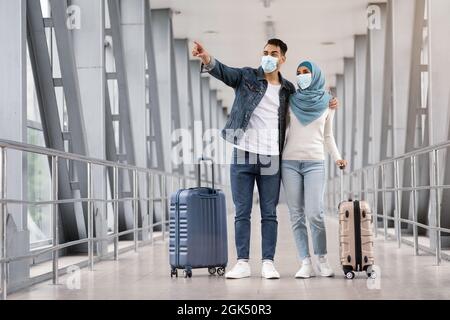 Jeunes conjoints islamiques portant des masques médicaux de protection debout avec des valises à l'aéroport Banque D'Images