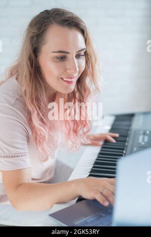 Une femme amicale joue le piano électronique et dirige un blog vidéo sur son ordinateur portable. Restez à la maison. Professeur d'instruments de musique. Musique d'apprentissage à distance Banque D'Images