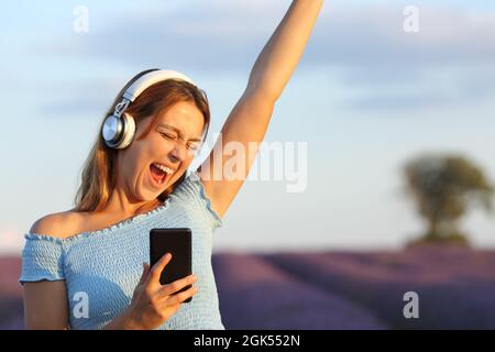 Bonne femme à écouter de la musique en portant des écouteurs et en chantant dans le champ de lavande Banque D'Images