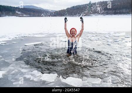 Vue de face d'une femme âgée active en maillot de bain barbotage d'eau à l'extérieur en hiver, concept de thérapie froide. Banque D'Images