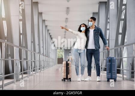 Jeunes conjoints du Moyen-Orient portant des masques médicaux attendant avec des valises à l'aéroport Banque D'Images