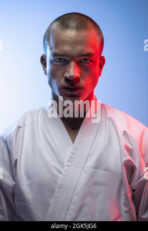 Image courte en gros plan d'un jeune sportif professionnel dans un kimono blanc isolé au-dessus d'un arrière-groupe bleu blanc. Karaté, judo, taekwondo sport Banque D'Images