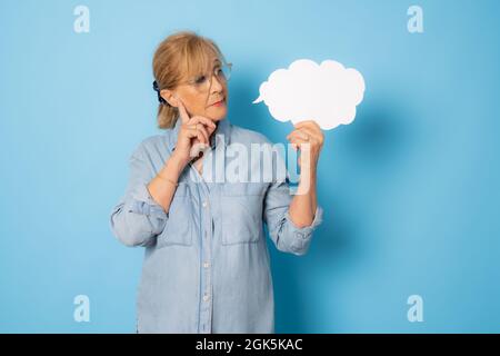 Femme âgée pensive tenant un signe blanc isolé sur fond bleu. Banque D'Images