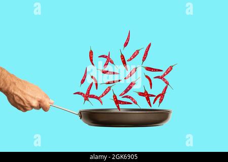 À la main avec une poêle et du piment fort sur fond bleu. Collage alimentaire, concept artistique créatif minimal. Photo de haute qualité Banque D'Images