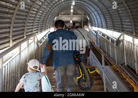 Un homme porte un vélo et un enfant. Le père dirige l'enfant et fait glisser son vélo dans la main. Monter les escaliers avec le bébé. Banque D'Images