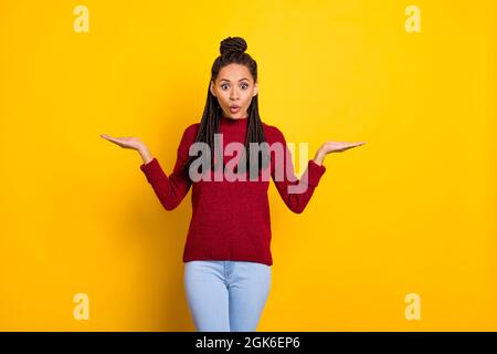 Photo de la drôle impressionnée peau sombre femme vêtue rouge chandail tenant les bras vide espace isolé couleur jaune fond Banque D'Images