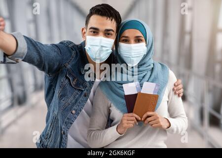 Heureux conjoints islamiques en masques médicaux de protection prenant Selfie à l'aéroport Banque D'Images