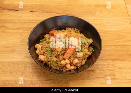 Riz aux fruits de mer sautés, surimi et coriandre à l'intérieur du bol noir sur une table en bois Banque D'Images