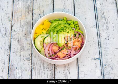 Un bol de poke au saumon mariné à la lime comme s'il s'agissait d'un ceviche avec des tranches d'avocat, des haricots édamames, des oignons violets, du concombre cru et de la mangue hachée. Banque D'Images