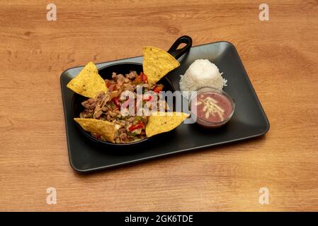 Ragoût de fil de bœuf mexicain avec poivrons et viande avec fromage, chips de maïs et riz avec sauce trempée sur plateau noir Banque D'Images