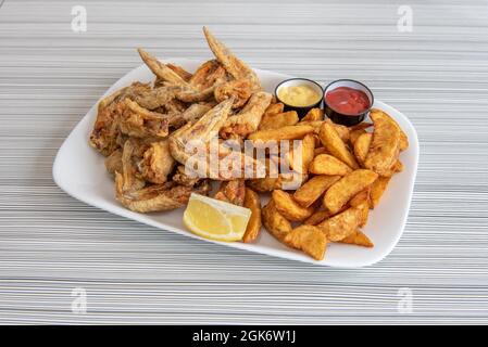 Grande portion d'ailes frites à l'huile d'olive garnie de frites fantaisie, citron pour la garniture et ketchup et moutarde pour la trempette Banque D'Images