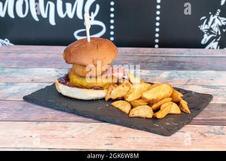 Hamburger américain avec sauce barbecue, veau couvert de fromage cheddar, bacon frit, oignon pané et coin de frites Banque D'Images