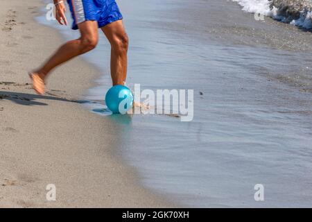 Les jambes d'un homme jouant au football sur la rive de la plage de Marina di Carrara, Toscane, Italie Banque D'Images