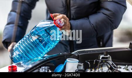 L'entraîneur mâle verse de l'antigel dans le réservoir pour vaporiser le pare-brise. Banque D'Images