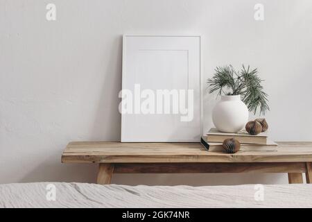 Maquette verticale de cadre d'image blanche. Banc en bois vintage, table. Vase moderne avec branches en pin. Boules en papier sur pile de livres. Mur blanc Banque D'Images