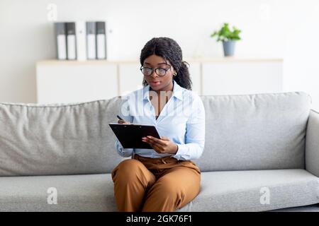 Portrait de la psychologue féminine noire ciblée prenant des notes dans le presse-papiers lors de la consultation au bureau Banque D'Images