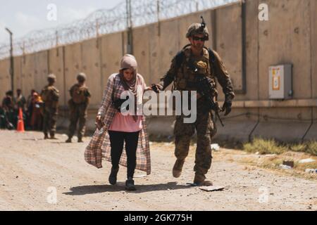 210822-M-TU241-1011 AÉROPORT INTERNATIONAL HAMID KARZAÏ (Afghanistan) (le 22 août 2021) Une Marine affectée à la 24e unité expéditionnaire maritime (UMM) assiste une femme lors d'une évacuation à l'aéroport international Hamid Karzaï, Kaboul (Afghanistan), le 22 août. Les membres du service américain aident le ministère d'État à effectuer une opération d'évacuation non combattantes (NEO) en Afghanistan. Banque D'Images