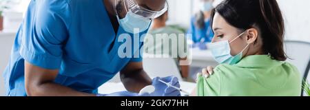 médecin afro-américain en masque médical vaccinant la jeune femme à l'hôpital, bannière Banque D'Images