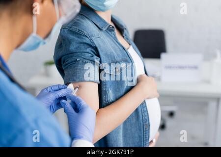 vue rognée d'une infirmière floue qui vaccine une femme enceinte en clinique Banque D'Images