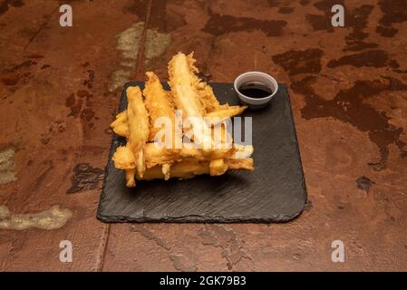 Lanières d'aubergines frites au tempura accompagnées d'un contenant de miel de canne à sucre sur une table métallique pelée Banque D'Images