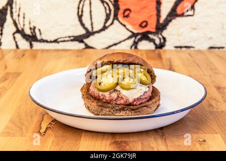 hamburger de bœuf avec pain de seigle, fromage bleu fondu et tranches de jalapeño sur une assiette blanche Banque D'Images