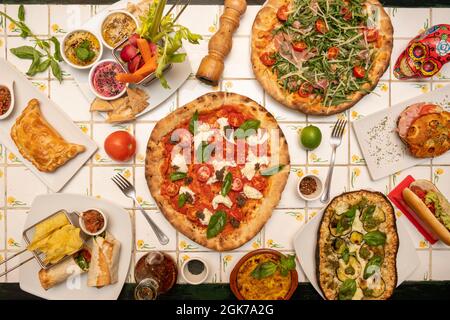 Vue de dessus des plats internationaux. Pizza au fromage de buffle et au basilic, houmous de diverses couleurs, burritos, empanadas argentines, aub rôti Banque D'Images