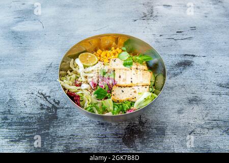 Bol en métal de salade végétalienne avec tofu en filets, graines de sésame, laitue variée, maïs doux, graines de tournesol, tranches de concombre et laitue d'agneau avec lim Banque D'Images