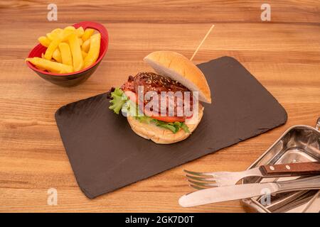 Hamburger de bœuf classique avec sauce barbecue, tomates en tranches, laitue et graines de sésame garnies de frites. Banque D'Images