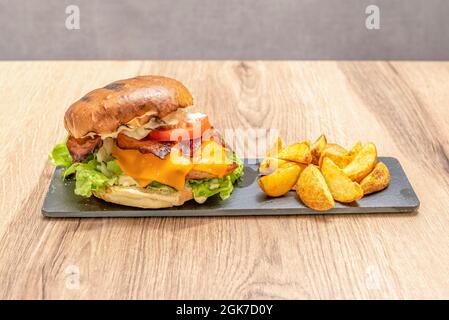 Hamburger au poulet avec fromage cheddar fondu, tranches de bacon frit, tranches de tomates et laitue avec mayonnaise et un côté de frites Banque D'Images