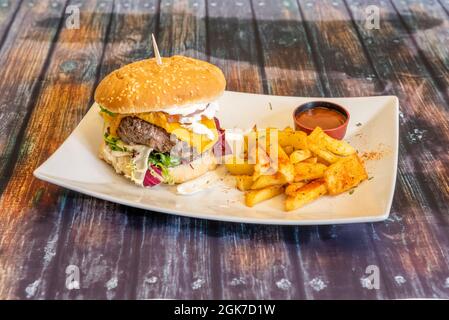 Hamburger avec un grand morceau de viande, fromage cheddar, mayonnaise, assortiment de laitue, tomate et cornichons, garni de frites avec paprika et ba Banque D'Images