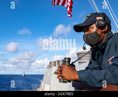 MER DES PHILIPPINES (août 28, 2021) le marin Gerrod Collins, de Miami, est à l'affût sur l'aile du pont du destroyer de missile guidé de classe Arleigh Burke USS Barry (DDG 52) comme Marine royale australienne HMAS Warramunga avec des navires de la Force d'autodéfense maritime du Japon et de la Marine indienne naviguent en formation pendant MALABAR 2021. Barry est actuellement déployé à l’appui du commandant de la Force opérationnelle (CTF) 71/Escadrier Squadron (DESRON) 15, le plus grand DESRON déployé à l’avant de la Marine et la principale force de surface de la 7e flotte américaine. Banque D'Images