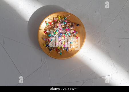 épingles à coudre de couleur dans une assiette dorée sur fond gris Banque D'Images