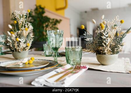 Décor rustique de table à manger : fleurs séchées dans un vase, verres en verre vert et assiettes en céramique Banque D'Images
