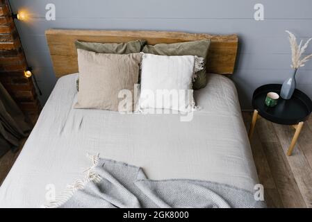 Un vase moderne en céramique blanche avec de l'herbe séchée et une tasse de café ou de thé à côté du lit double. Draps et oreillers gris dans la chambre, scandinave Banque D'Images