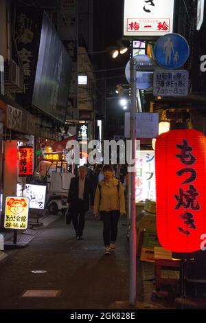 Piétons marchant dans une ruelle japonaise étroite la nuit, éclairée par des panneaux et des lanternes japonaises de chaque côté, Ryogoku, Tokyo, Japon Banque D'Images