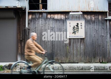 Cycliste japonais de sexe masculin âgé qui descend dans une petite rue à Kyoto, au Japon Banque D'Images